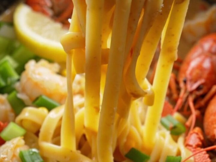 A close-up of creamy crawfish etouffee fettuccine served in a bowl, topped with green onions and lemon wedges.