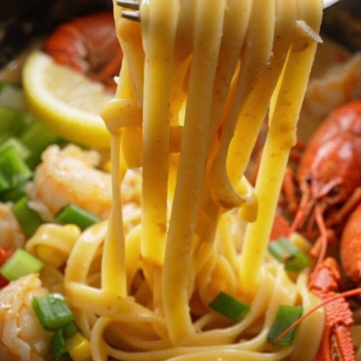 A close-up of creamy crawfish etouffee fettuccine served in a bowl, topped with green onions and lemon wedges.