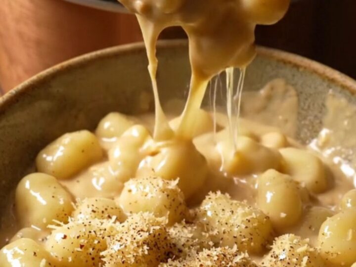 A close-up view of pillowy potato gnocchi covered in a thick, molten four-cheese cream sauce in a ceramic pot.