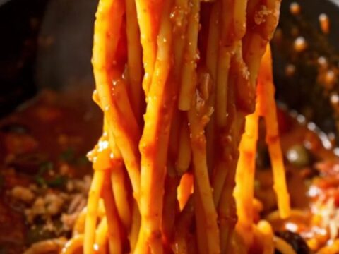 A bowl of spaghetti tossed with a rich, tomato-based Puttanesca sauce, topped with fresh basil and breadcrumbs.