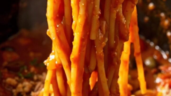A bowl of spaghetti tossed with a rich, tomato-based Puttanesca sauce, topped with fresh basil and breadcrumbs.