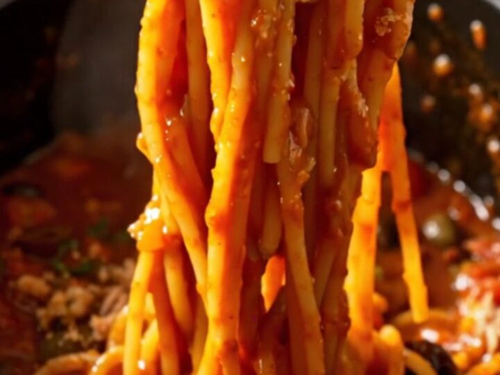 A bowl of spaghetti tossed with a rich, tomato-based Puttanesca sauce, topped with fresh basil and breadcrumbs.