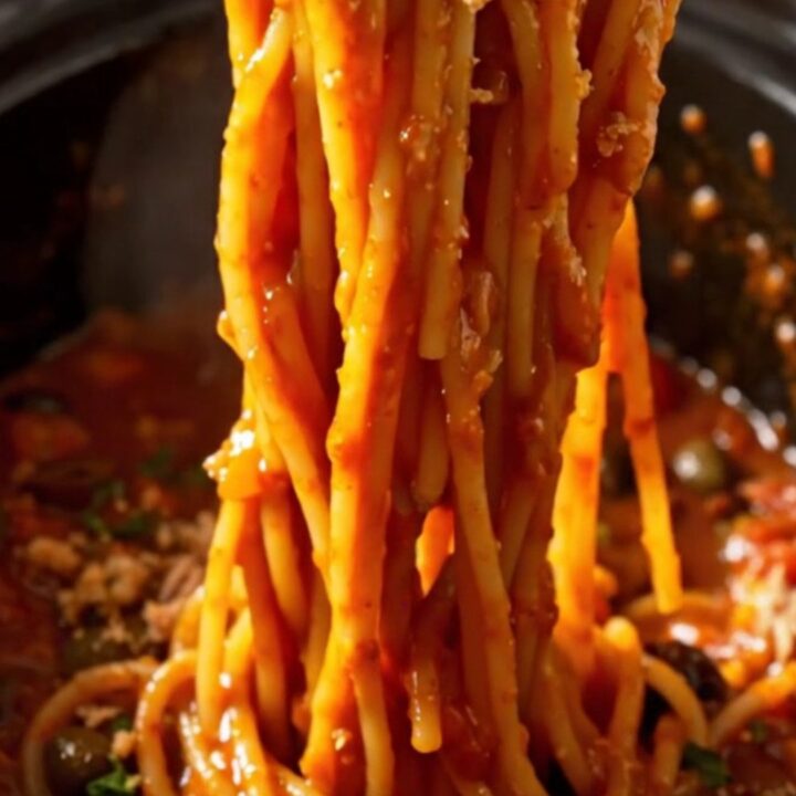 A bowl of spaghetti tossed with a rich, tomato-based Puttanesca sauce, topped with fresh basil and breadcrumbs.