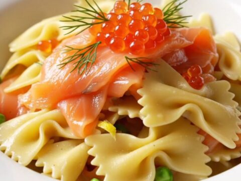 A close-up of a porcelain bowl filled with creamy farfalle pasta, smoked salmon ribbons, and fresh dill.