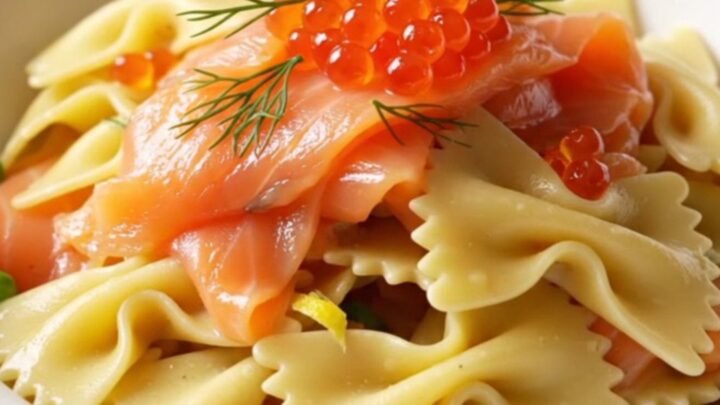 A close-up of a porcelain bowl filled with creamy farfalle pasta, smoked salmon ribbons, and fresh dill.