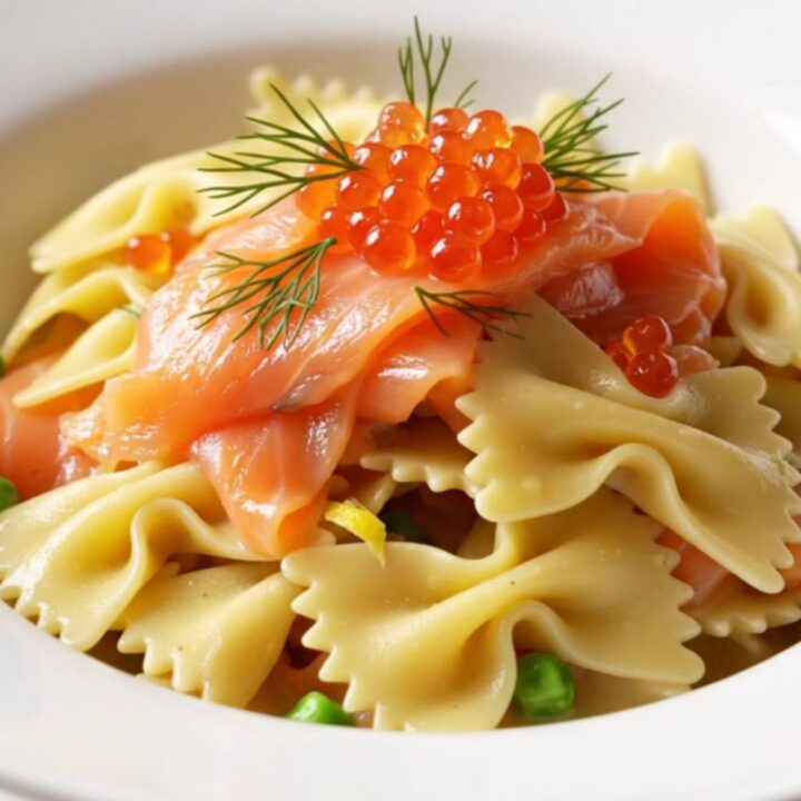 A close-up of a porcelain bowl filled with creamy farfalle pasta, smoked salmon ribbons, and fresh dill.