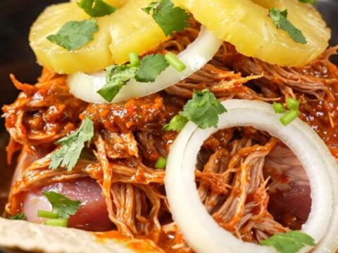 A red stoneware slow cooker filled with shredded Al Pastor pork, pineapple, and onions.