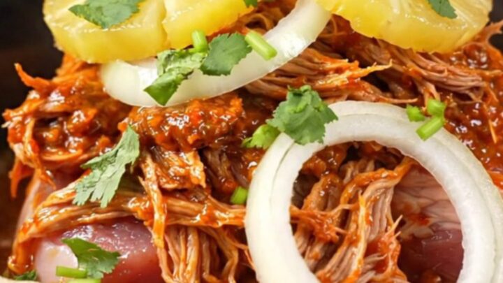 A red stoneware slow cooker filled with shredded Al Pastor pork, pineapple, and onions.