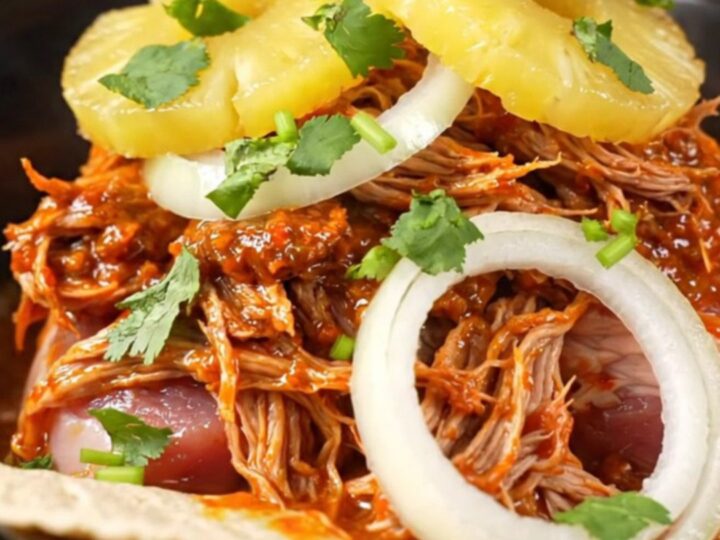 A red stoneware slow cooker filled with shredded Al Pastor pork, pineapple, and onions.