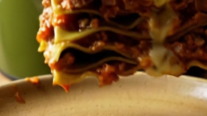 A close-up of a square of Lasagna Bolognese with visible layers of meat sauce, spinach pasta, and melted cheese.