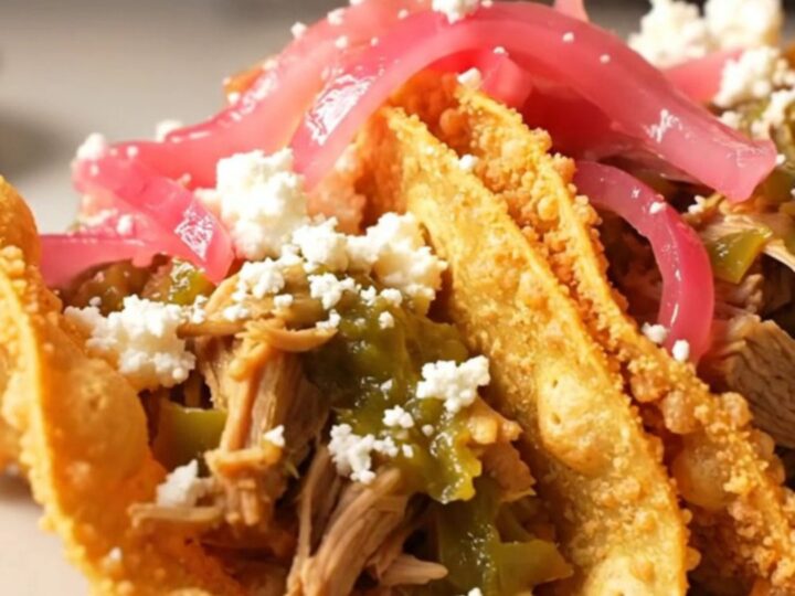 A close-up of tender pulled pork in a crockpot with vibrant green salsa verde and green chiles.