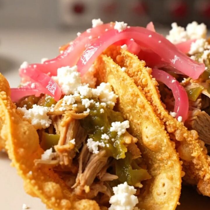 A close-up of tender pulled pork in a crockpot with vibrant green salsa verde and green chiles.