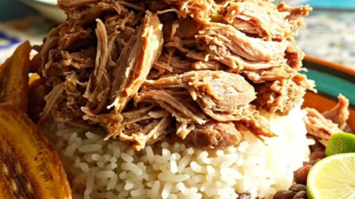 A close-up of tender shredded Cuban mojo pork glistening in a ceramic slow cooker with vibrant herb-infused juices.