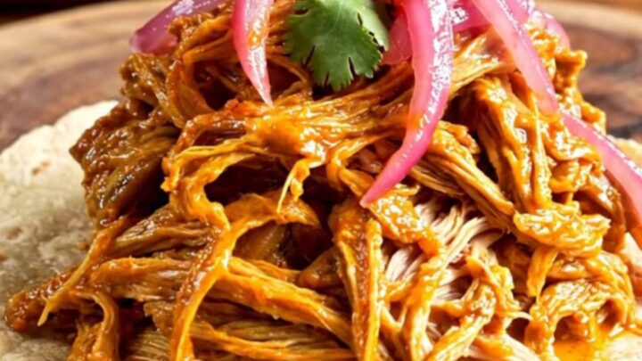 A steaming bowl of shredded Cochinita Pibil served on warm tortillas with pickled onions and cilantro.