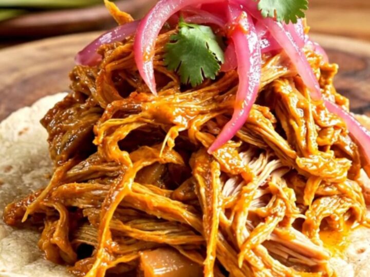 A steaming bowl of shredded Cochinita Pibil served on warm tortillas with pickled onions and cilantro.