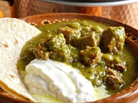 A rustic bowl of Green Chile Pork Chile Verde topped with crema and served with warm flour tortillas.
