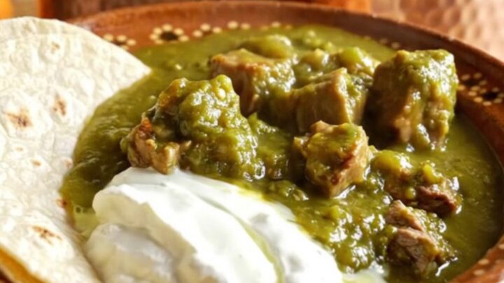 A rustic bowl of Green Chile Pork Chile Verde topped with crema and served with warm flour tortillas.