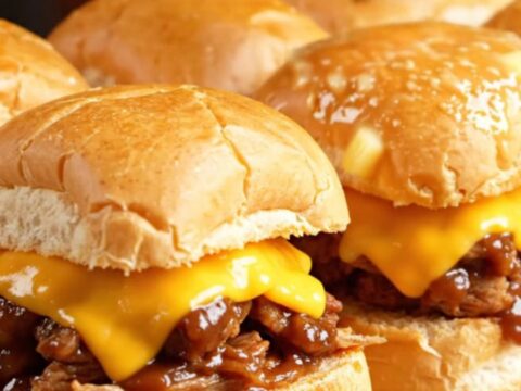 A close-up shot of Dr. Pepper and chipotle BBQ pulled pork sliders on Hawaiian rolls with melted cheese.