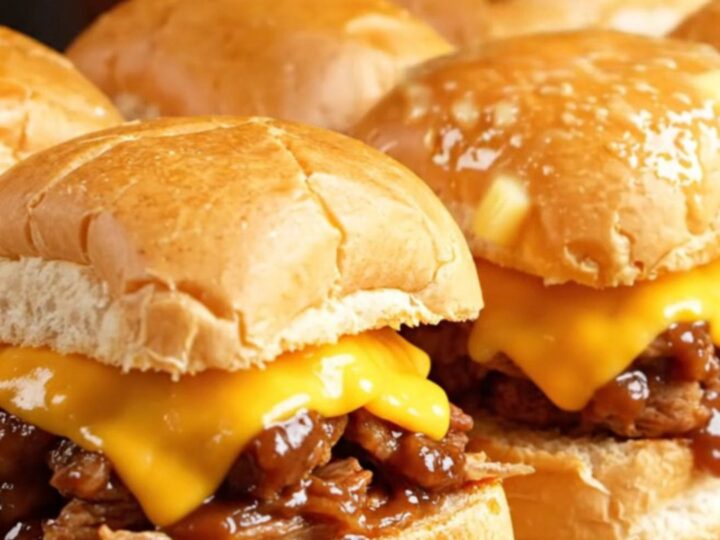 A close-up shot of Dr. Pepper and chipotle BBQ pulled pork sliders on Hawaiian rolls with melted cheese.