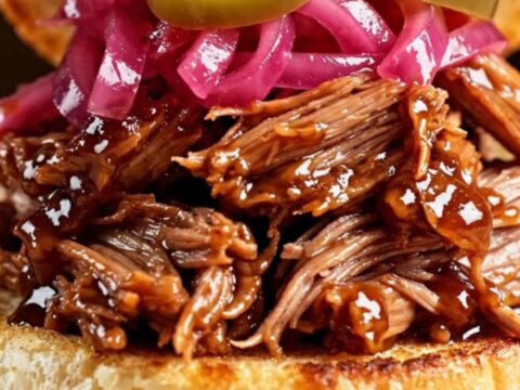 A glossy cherry-red slow cooker filled with tender, mahogany-colored pulled pork in a rich cherry glaze.