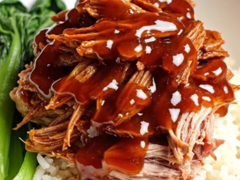 A close-up of tender, ruby-red shredded Char Siu pork glistening with a thick honey glaze.