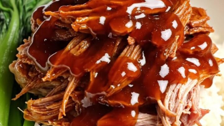 A close-up of tender, ruby-red shredded Char Siu pork glistening with a thick honey glaze.