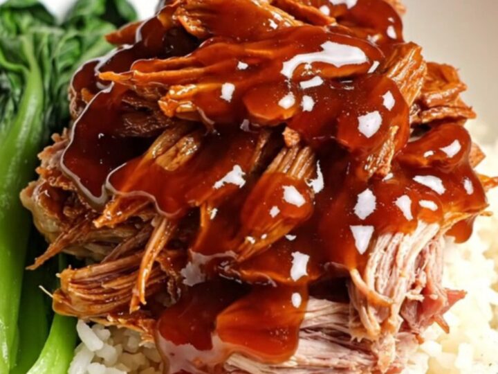 A close-up of tender, ruby-red shredded Char Siu pork glistening with a thick honey glaze.