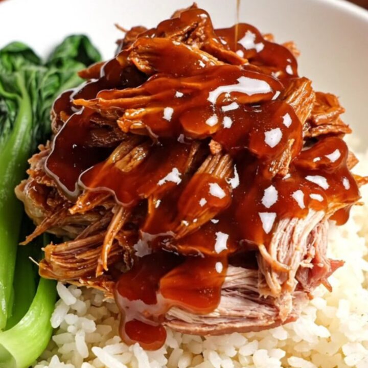 A close-up of tender, ruby-red shredded Char Siu pork glistening with a thick honey glaze.