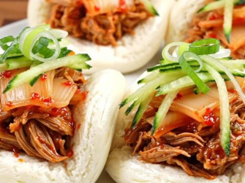 Glossy Korean gochujang pulled pork in a slow cooker with sesame seeds.