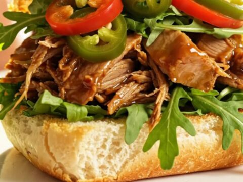 A close-up of a slow cooker filled with shredded pulled pork, caramelized peaches, and a rich, glossy bourbon glaze.