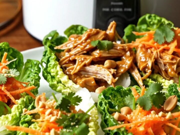 A ceramic slow cooker filled with shredded pulled pork covered in a glossy, rich peanut and sweet chili sauce.
