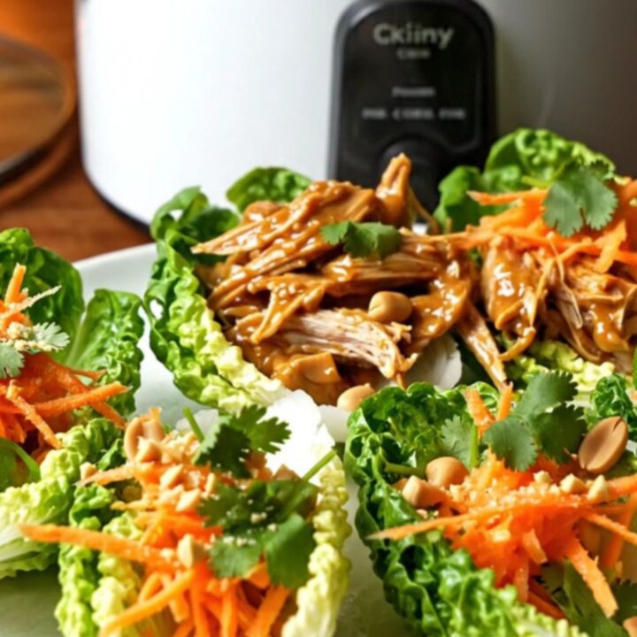 A ceramic slow cooker filled with shredded pulled pork covered in a glossy, rich peanut and sweet chili sauce.