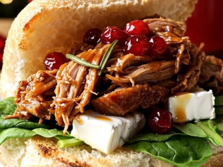 A close-up of a festive pulled pork slider on a rosemary ciabatta roll with melted brie and fresh spinach.