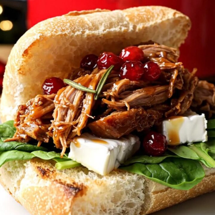 A close-up of a festive pulled pork slider on a rosemary ciabatta roll with melted brie and fresh spinach.