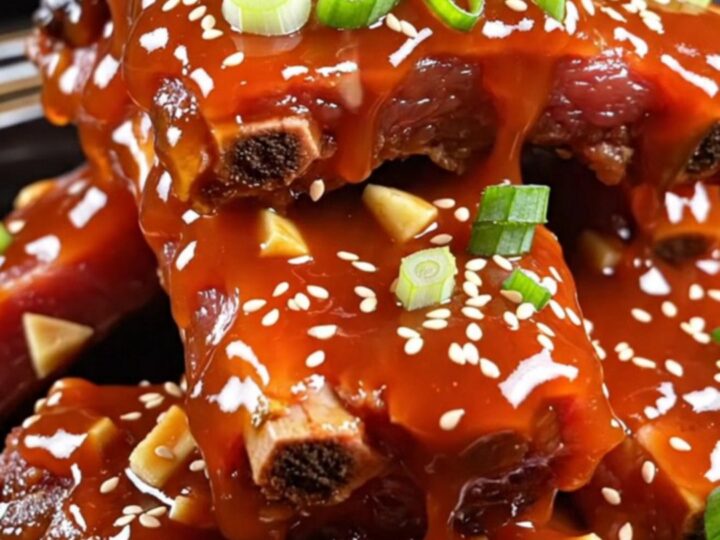 Sticky honey sriracha glazed pork ribs piled in a bowl and garnished with scallions and sesame seeds.