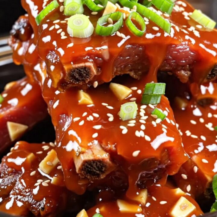 Sticky honey sriracha glazed pork ribs piled in a bowl and garnished with scallions and sesame seeds.