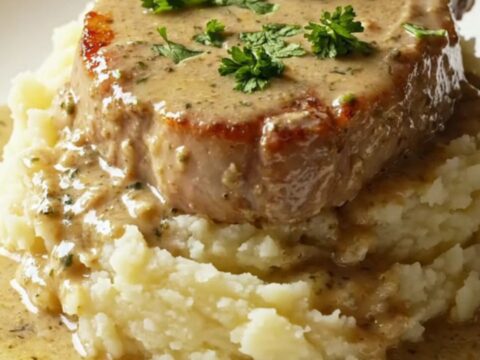 A succulent, golden-seared bone-in pork chop topped with creamy mushroom gravy on a plate.