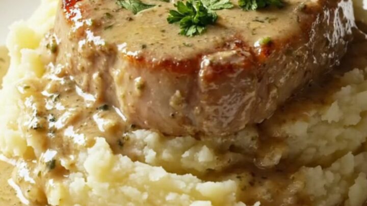 A succulent, golden-seared bone-in pork chop topped with creamy mushroom gravy on a plate.