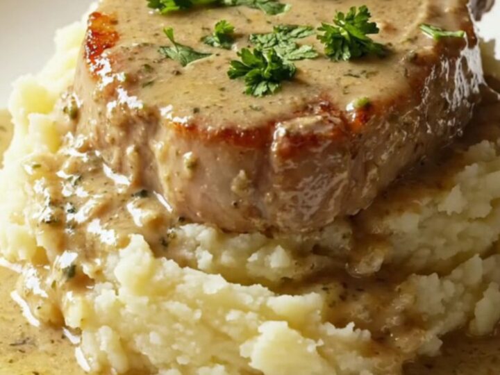 A succulent, golden-seared bone-in pork chop topped with creamy mushroom gravy on a plate.