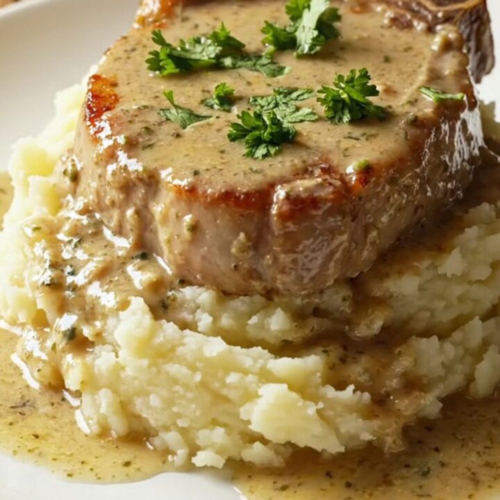 A succulent, golden-seared bone-in pork chop topped with creamy mushroom gravy on a plate.