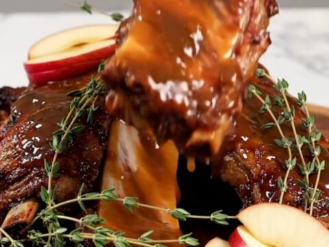 A close-up of tender, dark brown baby back ribs covered in a thick, glossy apple butter sauce on a wooden platter.