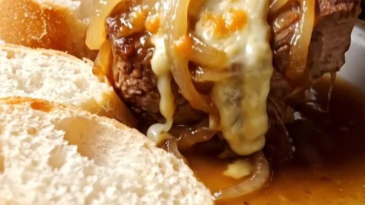 A close-up of a tender pork chop smothered in caramelized onions and bubbling melted Gruyere cheese on a plate.