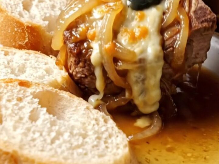 A close-up of a tender pork chop smothered in caramelized onions and bubbling melted Gruyere cheese on a plate.