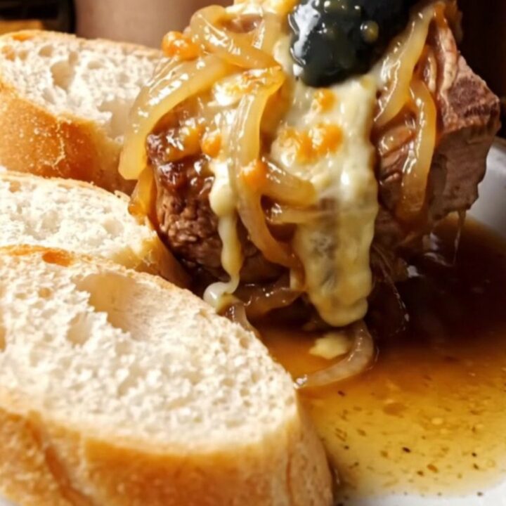 A close-up of a tender pork chop smothered in caramelized onions and bubbling melted Gruyere cheese on a plate.