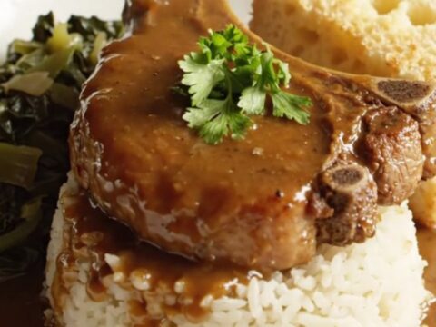 A close-up of tender bone-in pork chops smothered in a rich, dark brown onion gravy, served on a plate.