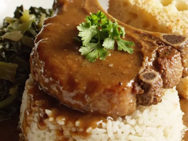 A close-up of tender bone-in pork chops smothered in a rich, dark brown onion gravy, served on a plate.