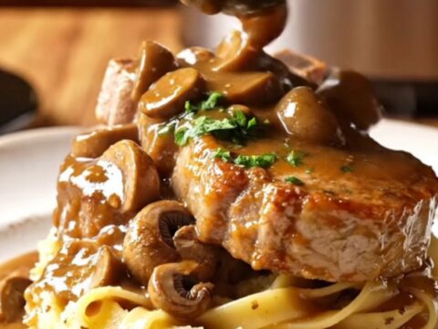 Close-up of succulent pork chops covered in a rich, creamy mushroom Marsala sauce in a black slow cooker.