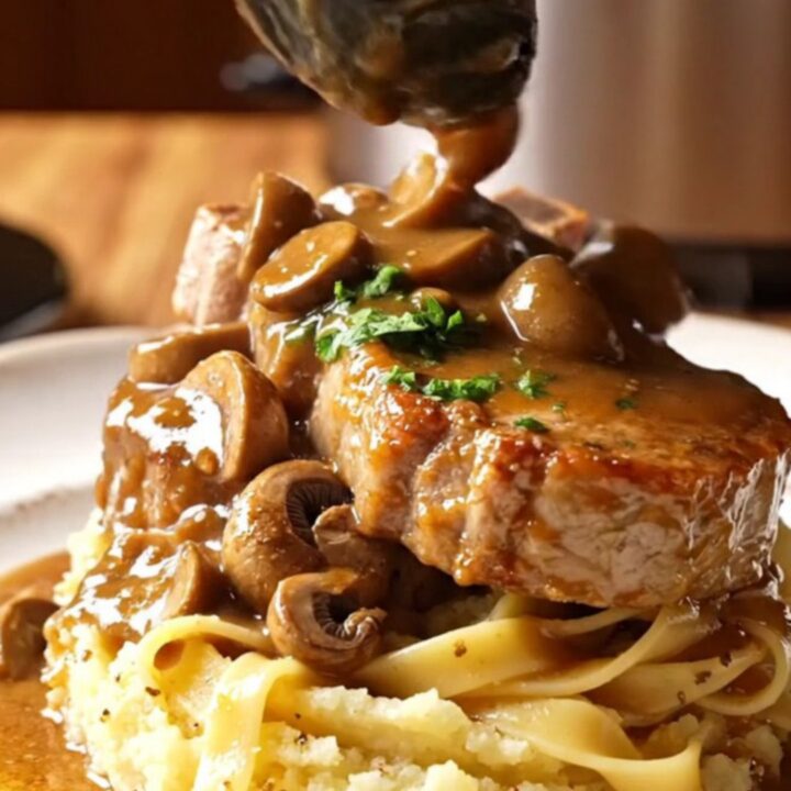 Close-up of succulent pork chops covered in a rich, creamy mushroom Marsala sauce in a black slow cooker.