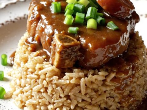 A close-up shot of Cajun smothered pork chops with sausage and vegetables in a red crockpot.