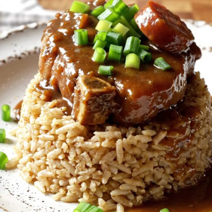 A close-up shot of Cajun smothered pork chops with sausage and vegetables in a red crockpot.